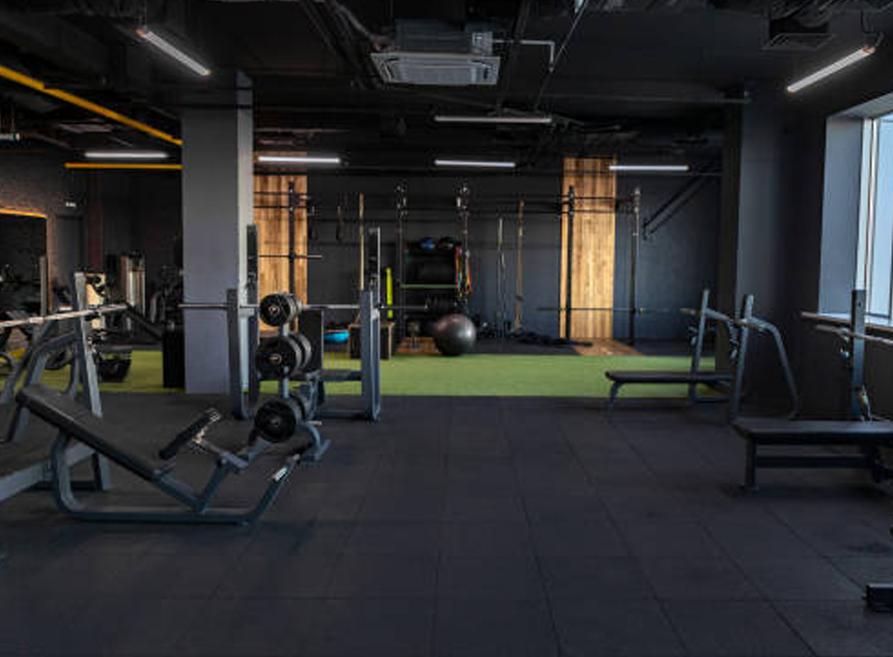 Modern gym interior with weight racks, dumbbells, and dark flooring under industrial lighting