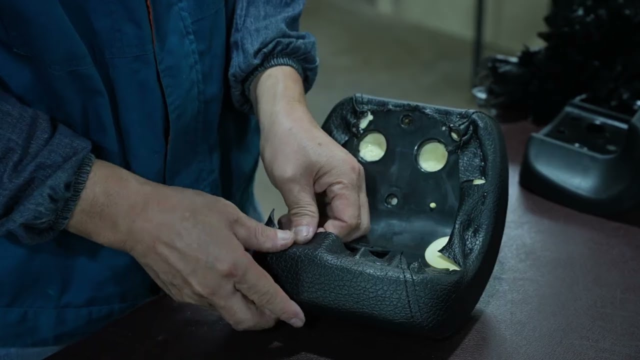 Close up of hands guiding black leather material through an industrial sewing machine